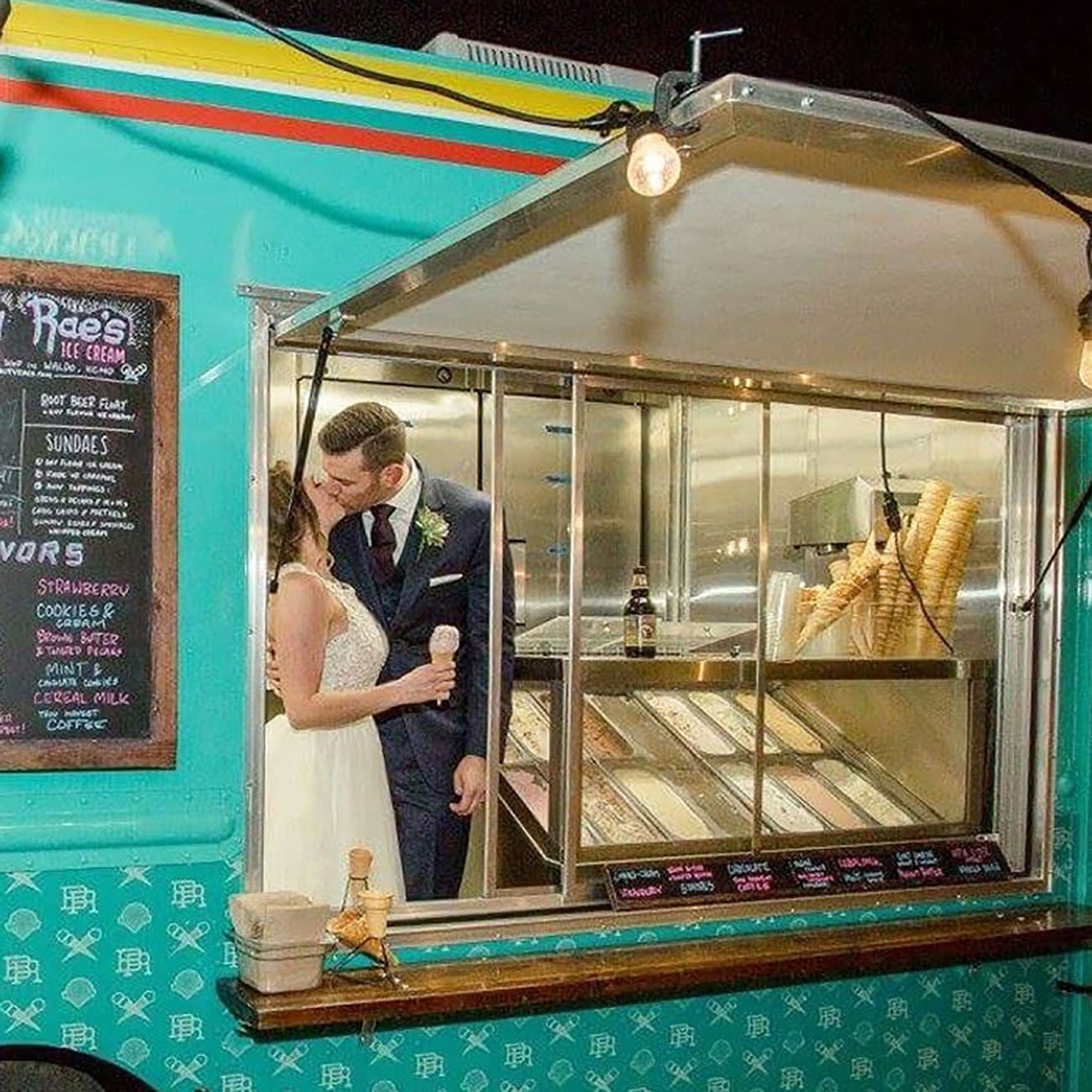 A bride and groom share a kiss while enjoying ice cream at a turquoise food truck during their wedding celebration. A bride and groom share a kiss while enjoying ice cream at a turquoise food truck during their wedding celebration.