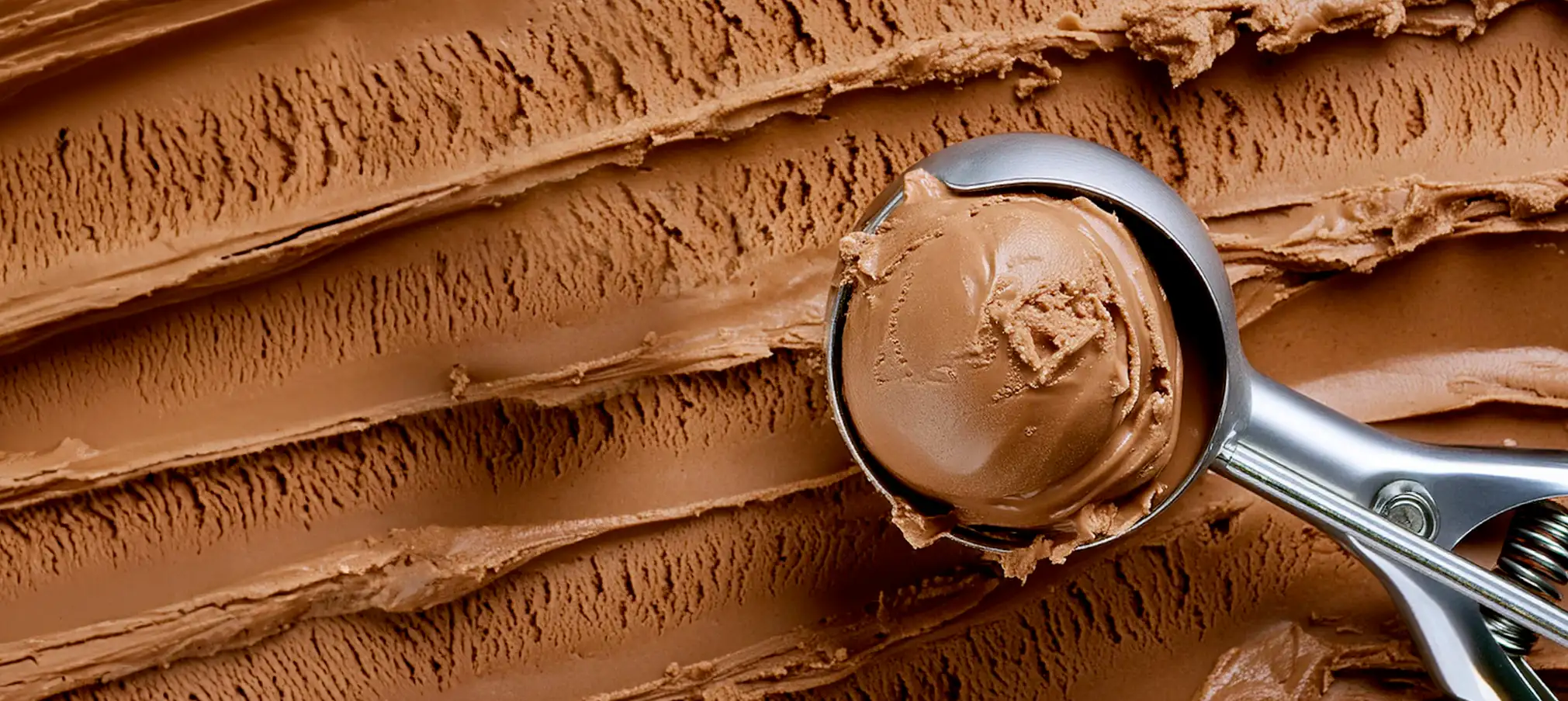 Scoop of creamy chocolate ice cream in a metal scooper over a textured chocolate ice cream background.